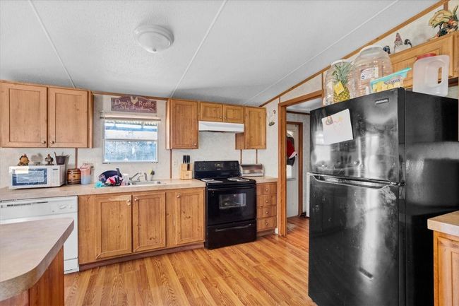 Kitchen with light countertops, light wood-style floors, a sink, under cabinet range hood, and black appliances | Image 9