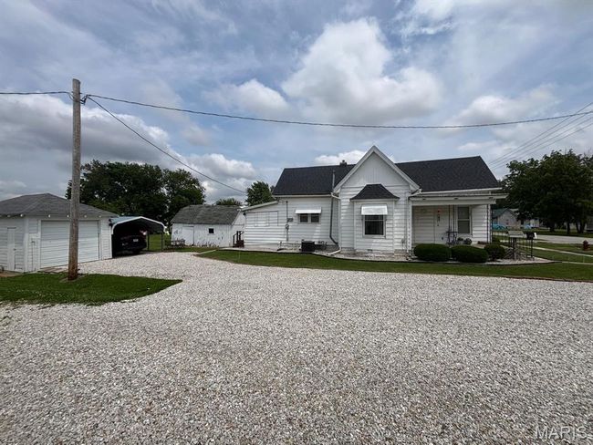 View of front facade with a detached carport, driveway, a porch, a shingled roof, and an outbuilding | Image 5