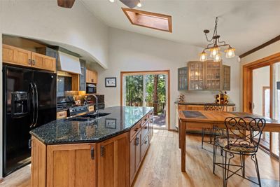 Kitchen with a kitchen island with sink, dark stone countertops, light wood-type flooring, black appliances, and hanging light fixtures | Image 3