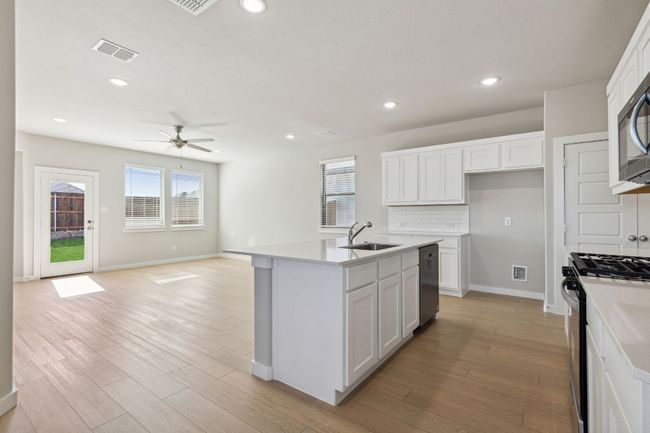 Kitchen with black range with gas stovetop, a sink, a ceiling fan, stainless steel dishwasher, and light wood-type flooring | Image 5
