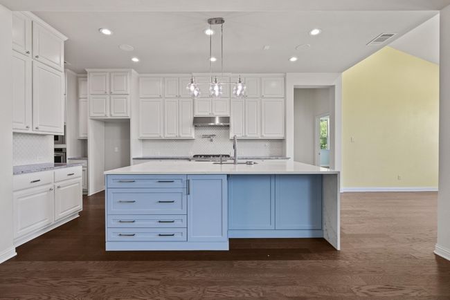 Kitchen featuring under cabinet range hood, white cabinetry, decorative backsplash, light countertops, and recessed lighting | Image 5