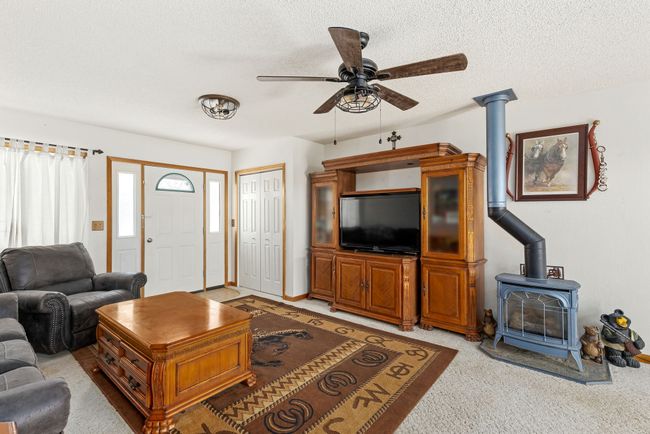 Living room featuring a textured ceiling, a wood stove, a ceiling fan, and light colored carpet | Image 37