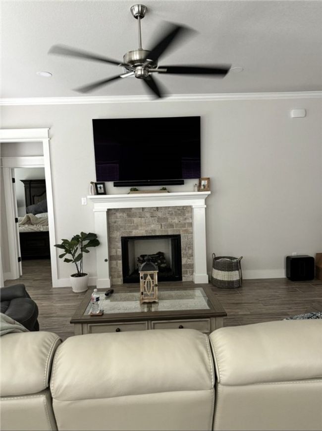 Living room with ornamental molding, ceiling fan, wood finished floors, and a fireplace with raised hearth | Image 14