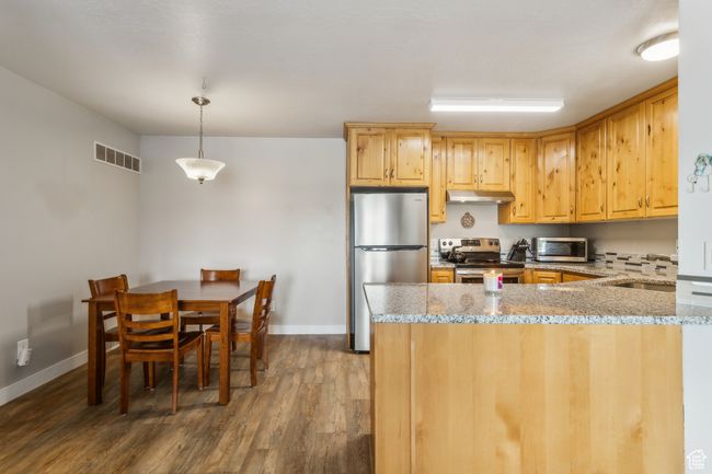 Kitchen with stainless steel appliances, under cabinet range hood, dark wood-type flooring, a peninsula, and light stone counters | Image 4