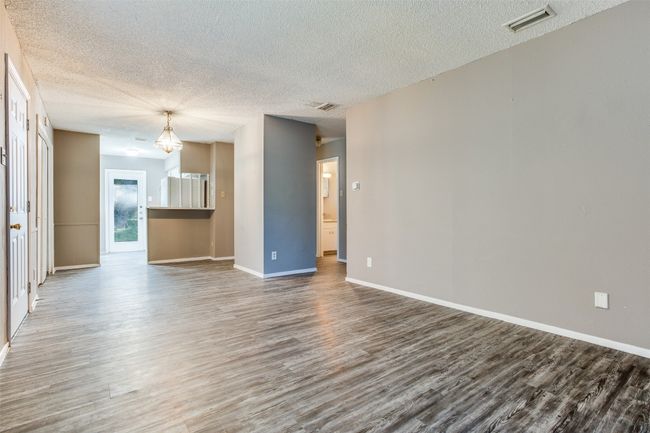 Unfurnished living room featuring a textured ceiling, baseboards, wood finished floors, and visible vents | Image 5