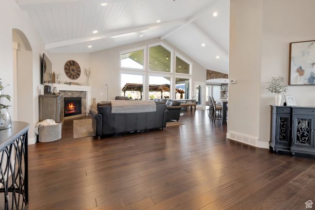 Living room featuring a lit fireplace, dark wood-style floors, beamed ceiling, high vaulted ceiling, and arched walkways | Image 6