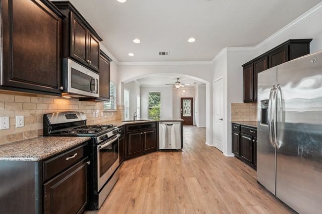Kitchen with appliances with stainless steel finishes, arched walkways, a sink, light wood finished floors, and dark brown cabinets | Image 14