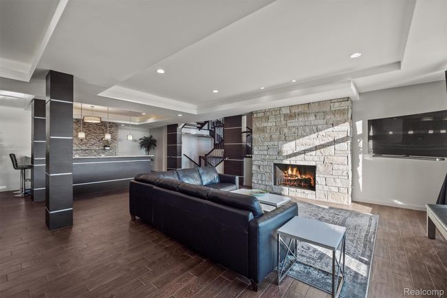 Living area with a tray ceiling, dark wood-type flooring, recessed lighting, and a stone fireplace | Image 24