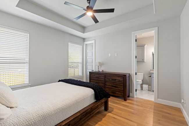 Bedroom with light wood finished floors, a tray ceiling, ensuite bath, baseboards, and ceiling fan | Image 22