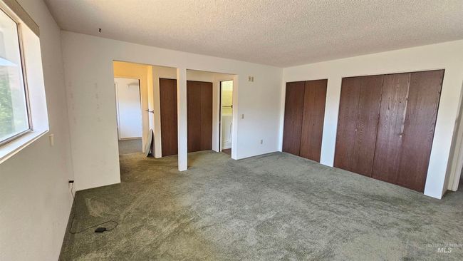 Unfurnished bedroom with two closets, carpet, and a textured ceiling | Image 15
