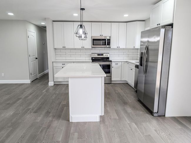 Kitchen with wood finished floors, appliances with stainless steel finishes, a kitchen island, and backsplash | Image 9