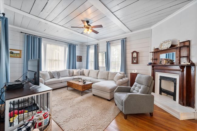 Living room featuring plenty of natural light, wood finished floors, ceiling fan, wooden ceiling with exposed beams, and a fireplace with raised hearth | Image 8