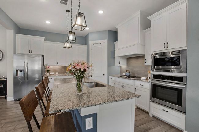Kitchen with stainless steel appliances, wood finished floors, white cabinetry, a sink, and a breakfast bar area | Image 8