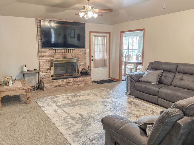 Living room with a brick fireplace, a ceiling fan, carpet, and baseboards | Image 11