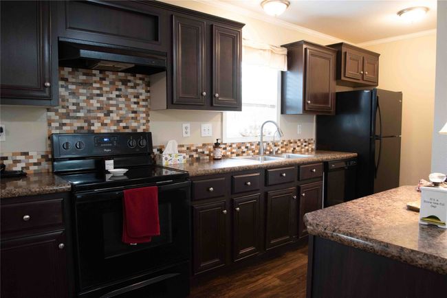 Kitchen featuring a sink, ornamental molding, under cabinet range hood, black appliances, and decorative backsplash | Image 21