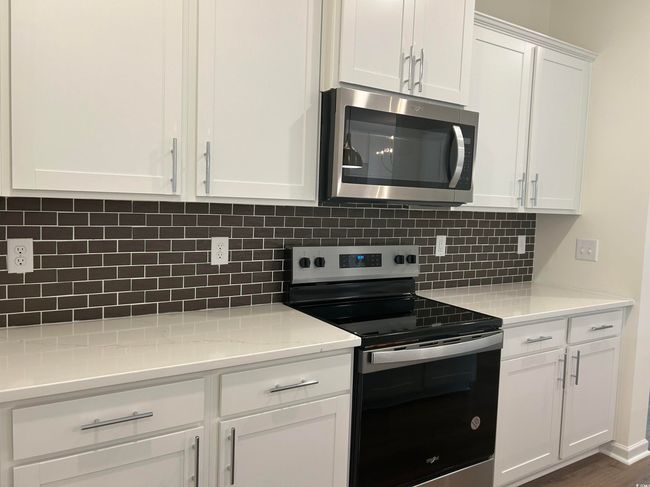 Kitchen with stainless steel appliances, white cabinetry, decorative backsplash, and light countertops | Image 5