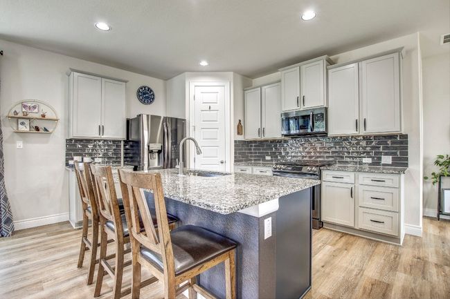 Kitchen with appliances with stainless steel finishes, light wood-type flooring, a center island with sink, light stone counters, and recessed lighting | Image 9
