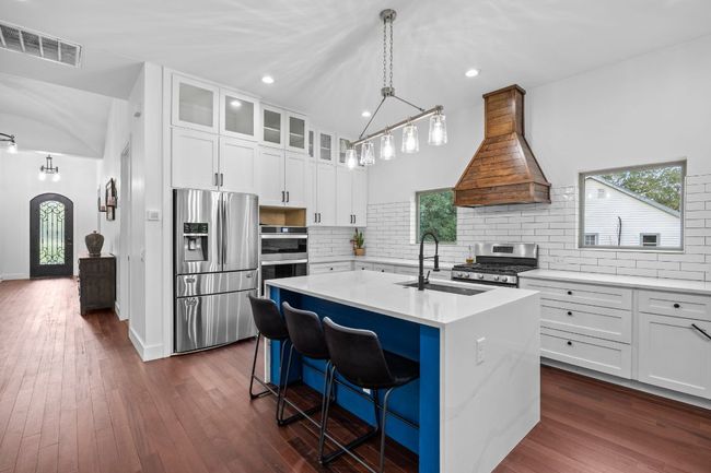 Kitchen with appliances with stainless steel finishes, custom exhaust hood, light countertops, an island with sink, and white cabinets | Image 8