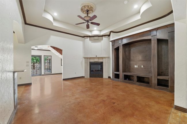 Unfurnished living room with a ceiling fan, a glass covered fireplace, a raised ceiling, baseboards, and arched walkways | Image 7