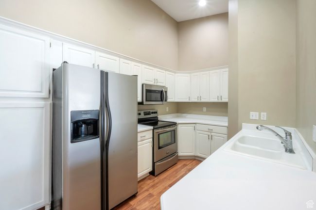 Kitchen featuring appliances with stainless steel finishes, light wood-type flooring, white cabinetry, light countertops, and a high ceiling | Image 6