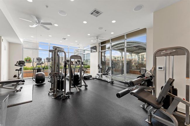This photo showcases a modern, well-lit gym with large windows, featuring various exercise equipment including cardio machines and weight stations. The space is inviting, with a view of surrounding buildings and greenery. | Image 30