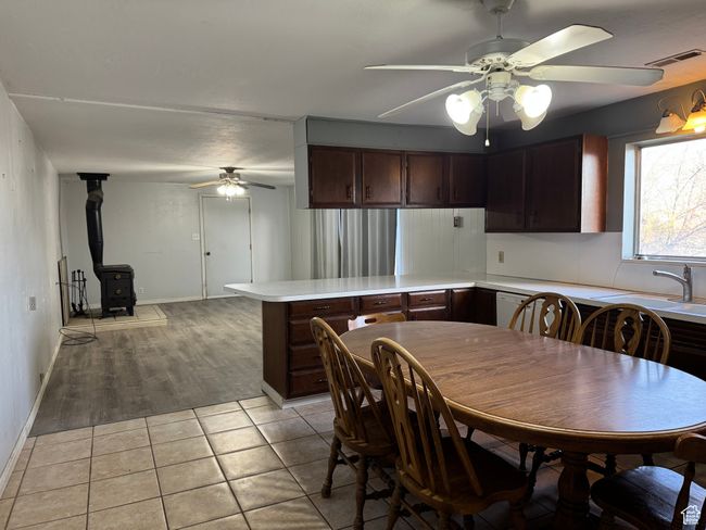 Dining area with a ceiling fan, a wood stove, light tile patterned floors, and baseboards | Image 8