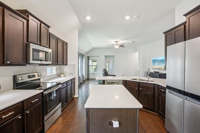 Kitchen with a center island, a sink, dark brown cabinets, light countertops, and appliances with stainless steel finishes | Image 12