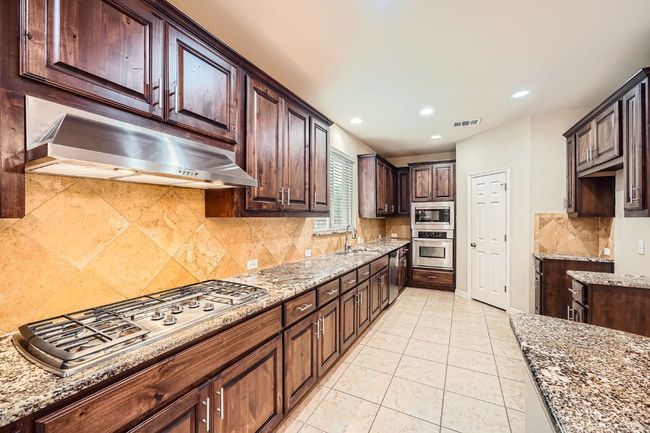 Kitchen with stainless steel appliances, exhaust hood, light stone countertops, decorative backsplash, and recessed lighting | Image 11