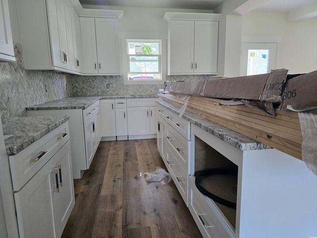 Kitchen featuring dark wood-type flooring, decorative backsplash, white cabinetry, and light stone counters | Image 10
