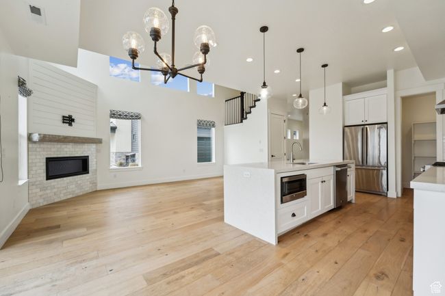 Kitchen with light wood finished floors, open floor plan, white cabinets, stainless steel appliances, and a sink | Image 12