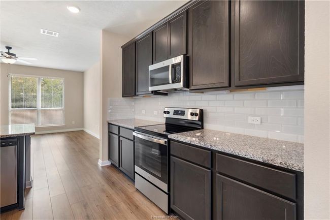 Kitchen with appliances with stainless steel finishes, a ceiling fan, backsplash, dark brown cabinetry, and light stone counters | Image 10