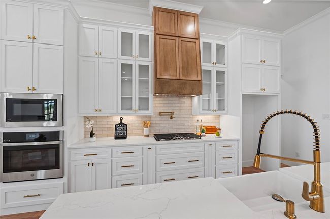 This kitchen boasts elegant cabinetry, a modern gas cooktop, and sleek stainless-steel appliances, complemented by a stylish farmhouse sink and warm wooden accents. Perfect for culinary enthusiasts! | Image 14