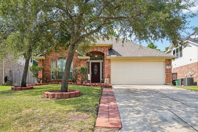 Charming brick home with a welcoming front yard featuring mature trees and landscaped flower beds. It has a spacious driveway leading to a two-car garage, and an elegant front entrance with a decorative glass door. | Image 29