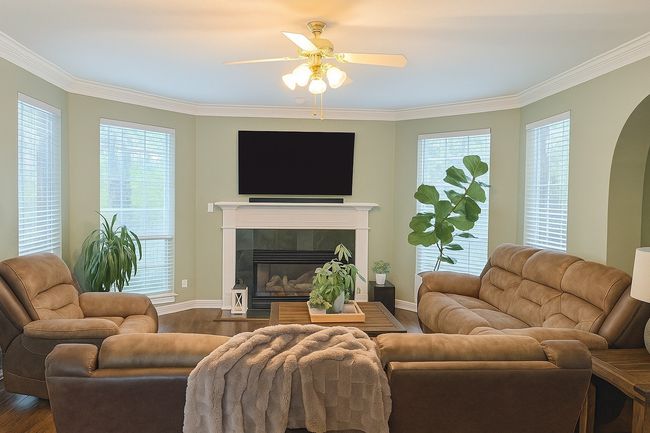 Living room featuring dark wood-style floors, a tiled fireplace, ceiling fan, ornamental molding, and arched walkways | Image 12