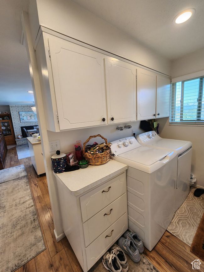 Washroom with cabinet space, a brick fireplace, washing machine and dryer, and hardwood / wood-style flooring | Image 14