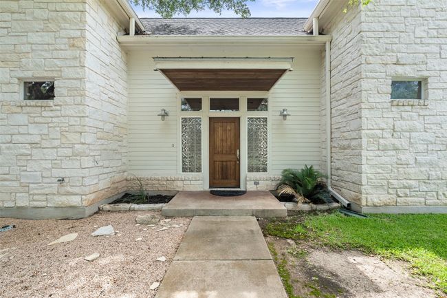 Doorway to property featuring a shingled roof and stone siding | Image 6