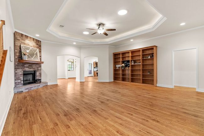 Unfurnished living room with visible vents, arched walkways, ceiling fan, light wood-type flooring, and a tray ceiling | Image 4