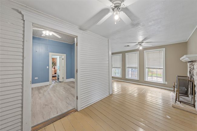 Unfurnished living room with ceiling fan, hardwood / wood-style flooring, a stone fireplace, and crown molding | Image 20