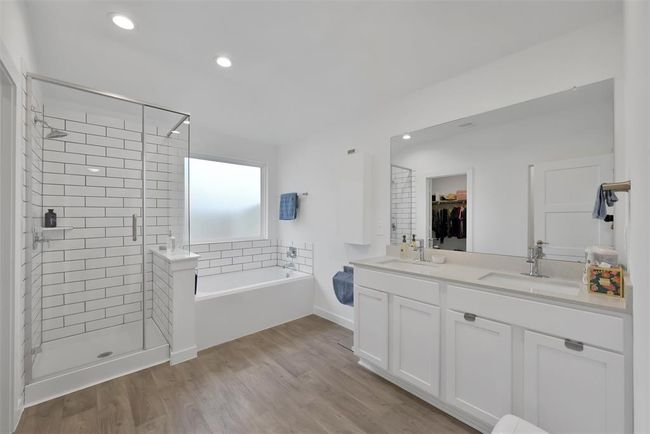 This modern bathroom features a spacious layout with a glass-enclosed shower and a separate bathtub. It includes a double vanity with ample storage, sleek white cabinetry, and wood-look flooring, creating a clean and inviting atmosphere. | Image 14