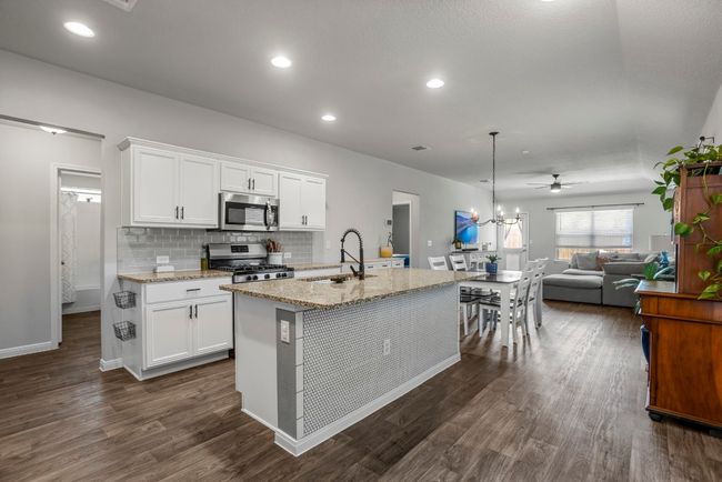 Kitchen with appliances with stainless steel finishes, dark wood-style flooring, light stone counters, ceiling fan, and a center island with sink | Image 6