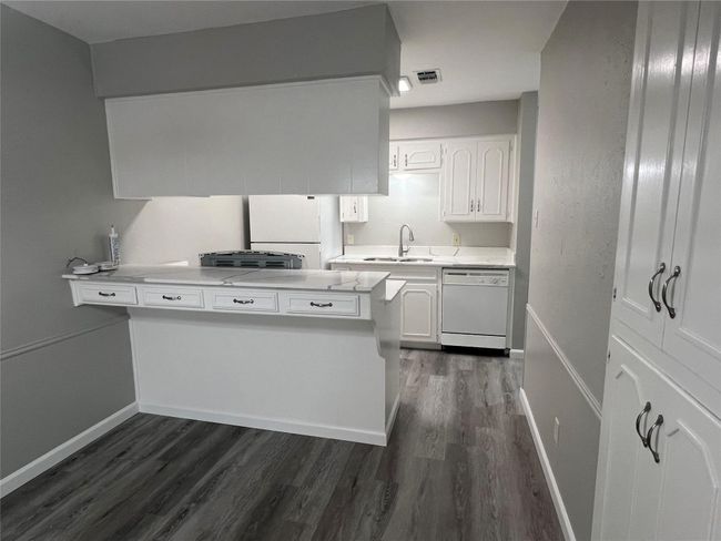 Kitchen with white appliances, white cabinets, dark wood-type flooring, a peninsula, and light countertops | Image 5