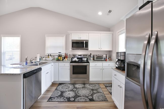 Kitchen with appliances with stainless steel finishes, a peninsula, vaulted ceiling, light wood-type flooring, and white cabinetry | Image 12