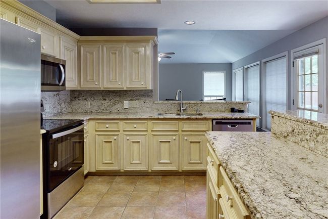 Kitchen with appliances with stainless steel finishes, a sink, a ceiling fan, decorative backsplash, and light tile patterned flooring | Image 11