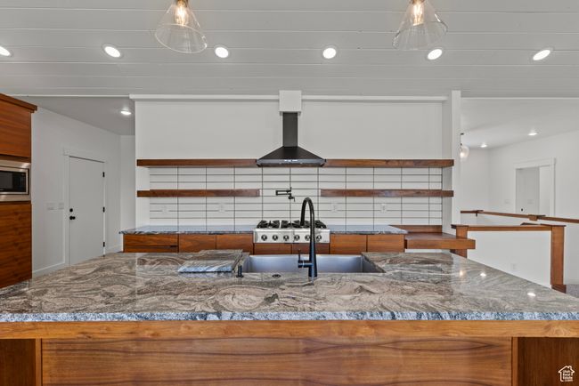 Kitchen with open shelves, brown cabinets, wall chimney range hood, stainless steel microwave, and recessed lighting | Image 7