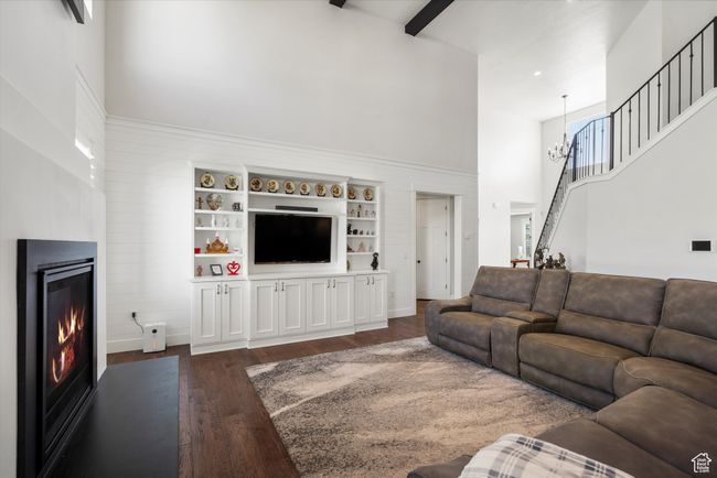 Living area featuring an inviting chandelier, a high ceiling, stairs, dark wood-type flooring, and a glass covered fireplace | Image 10