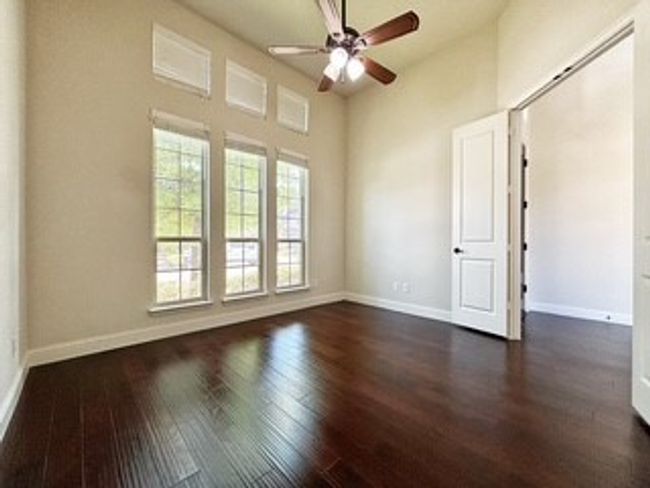 Empty room with dark wood finished floors, ceiling fan, and a high ceiling | Image 11