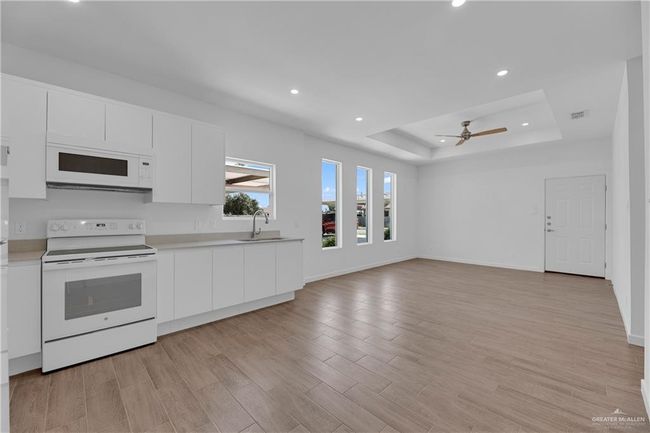 Kitchen with white cabinetry, sink, light hardwood / wood-style flooring, white appliances, and a tray ceiling | Image 4