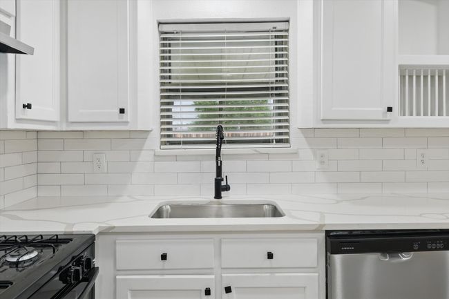 Kitchen featuring stainless steel dishwasher, a sink, white cabinetry, decorative backsplash, and extractor fan | Image 9