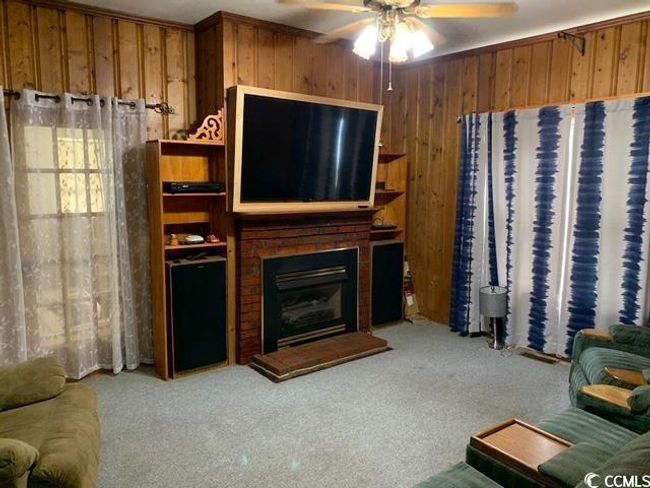 Living room with carpet flooring, wood walls, ceiling fan, and a brick fireplace | Image 16