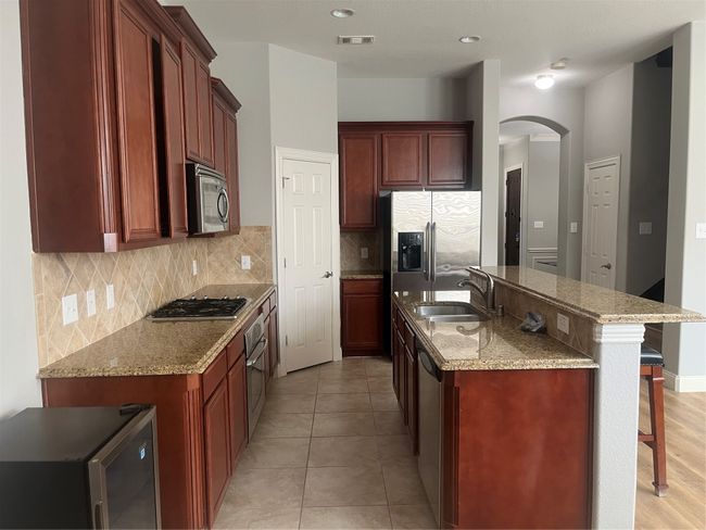 Kitchen featuring cooktop, arched walkways, a breakfast bar area, decorative backsplash, and a kitchen island with sink | Image 8